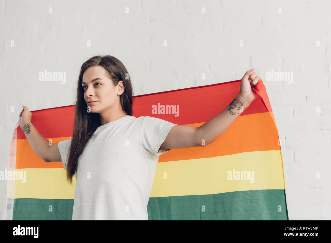 transgender man holding pride flag in front of white brick wall Stock Photo