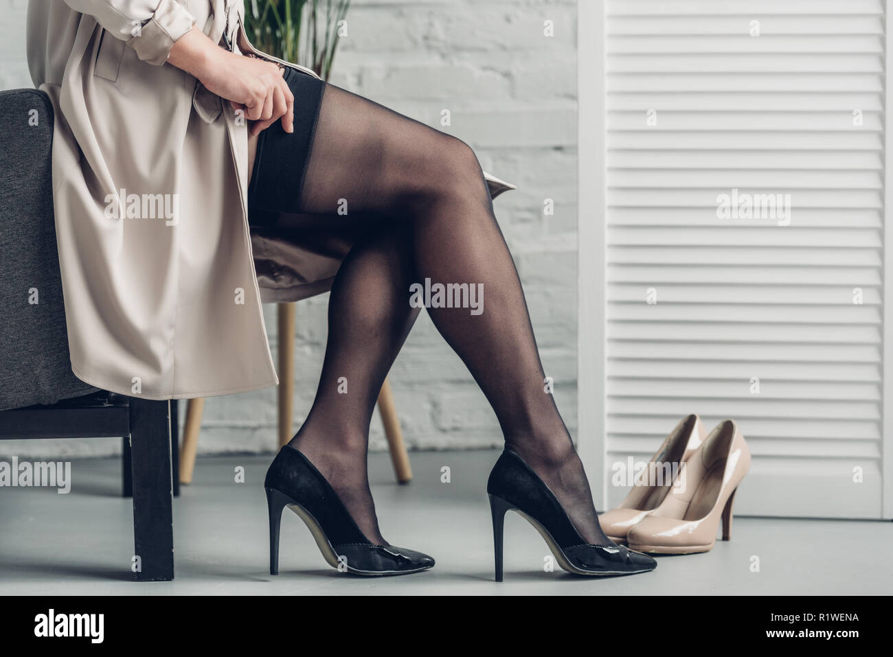 cropped shot of trans man in trench coat putting on stockings Stock Photo