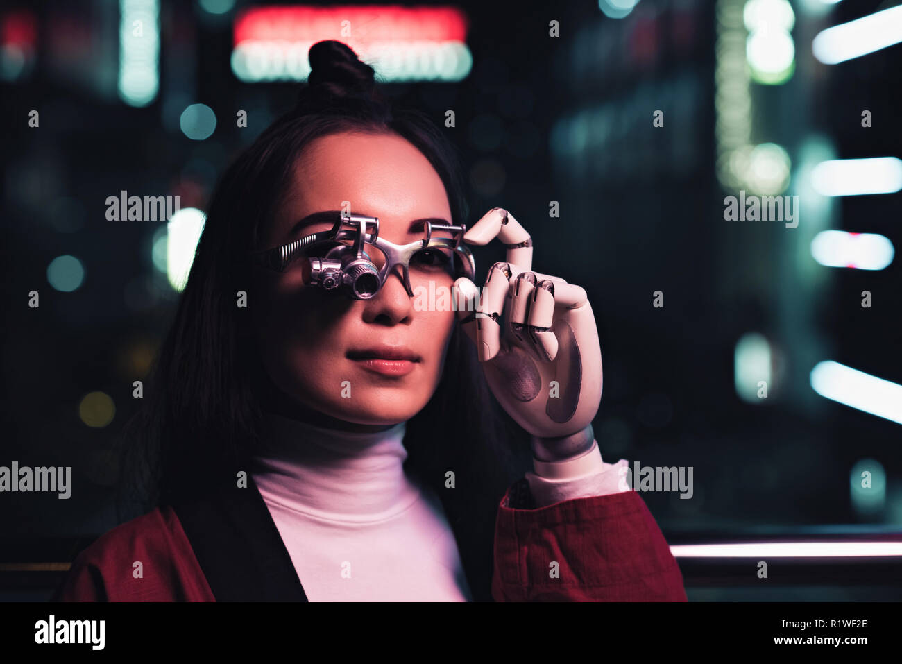 attractive asian girl with futuristic arm and eye prosthesis on street in evening, city of future concept Stock Photo