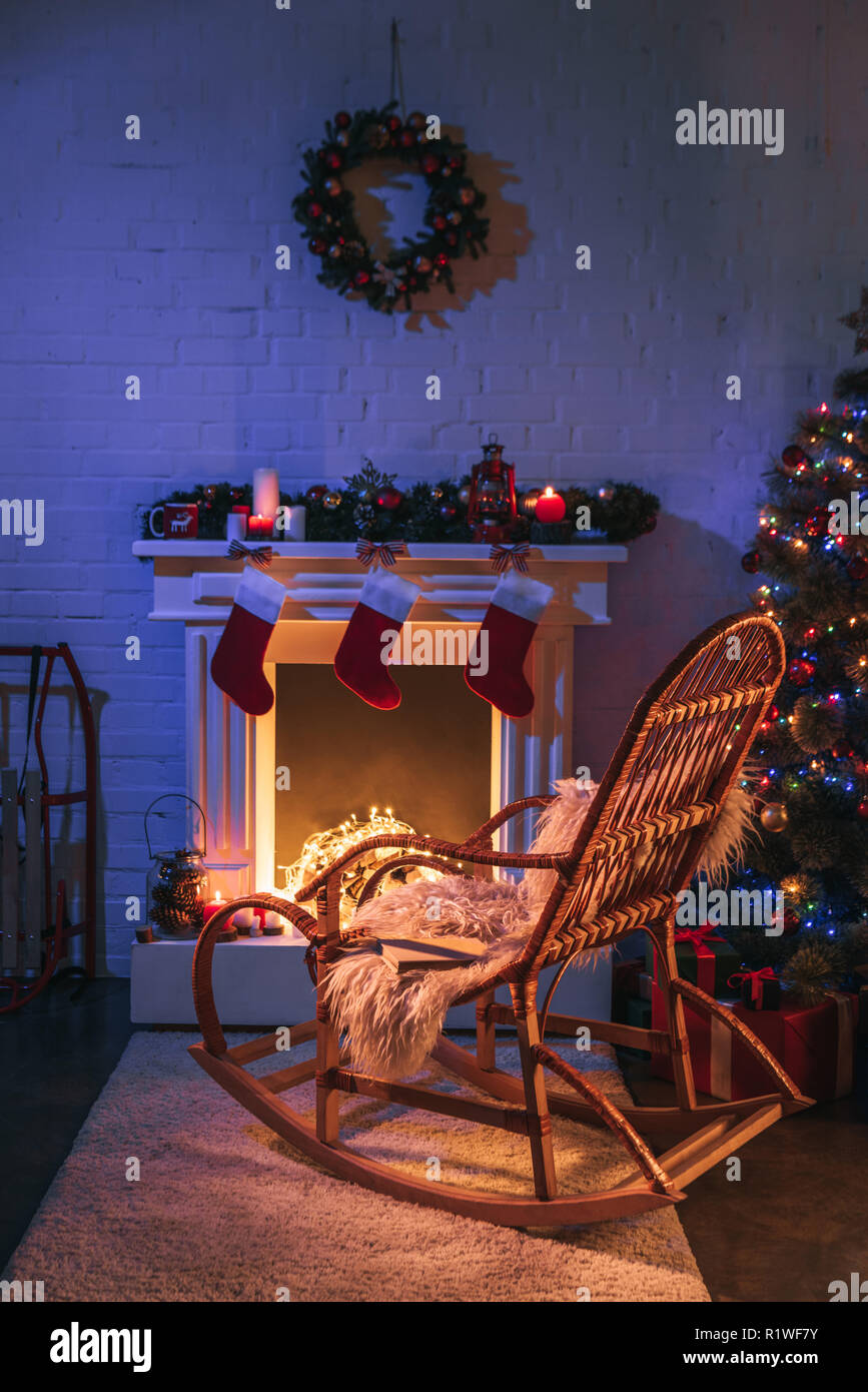 Fireplace with Christmas decorations near Christmas tree and wooden rocking chair Stock Photo