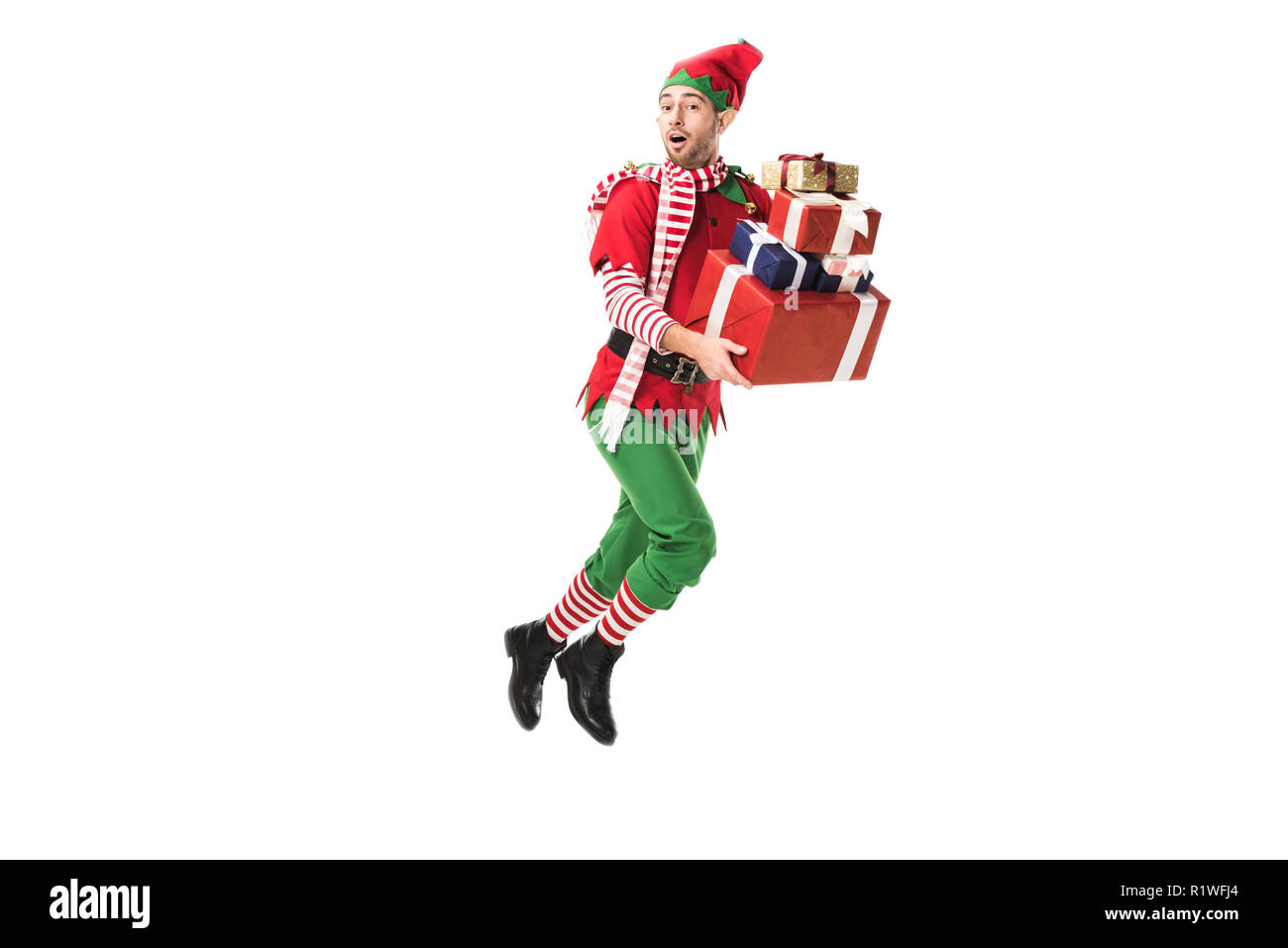 surprised man in christmas elf costume jumping and carrying pile of presents isolated on white Stock Photo