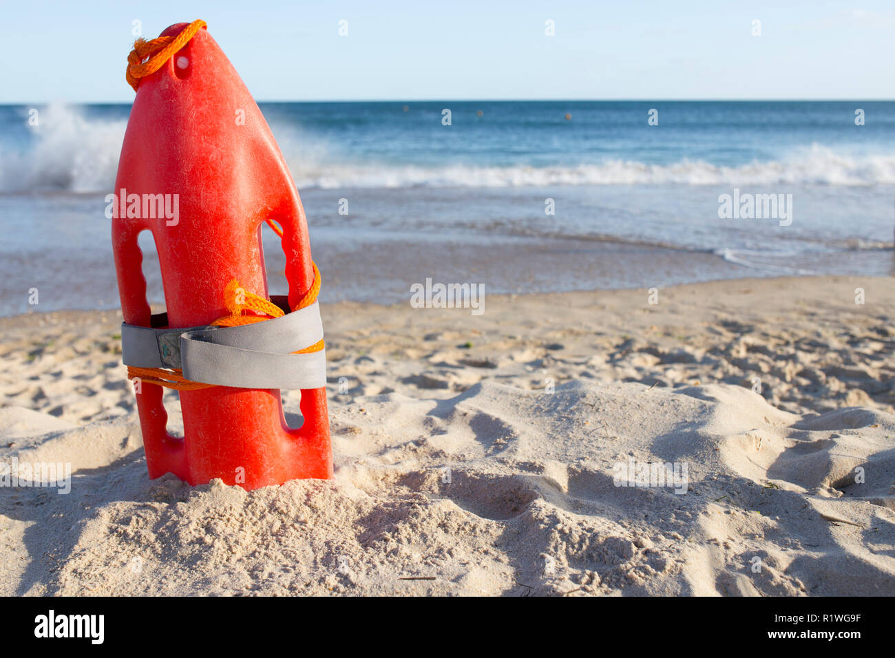 Orange rescue buoy planted on sand beach. Sea weaves as background Stock Photo