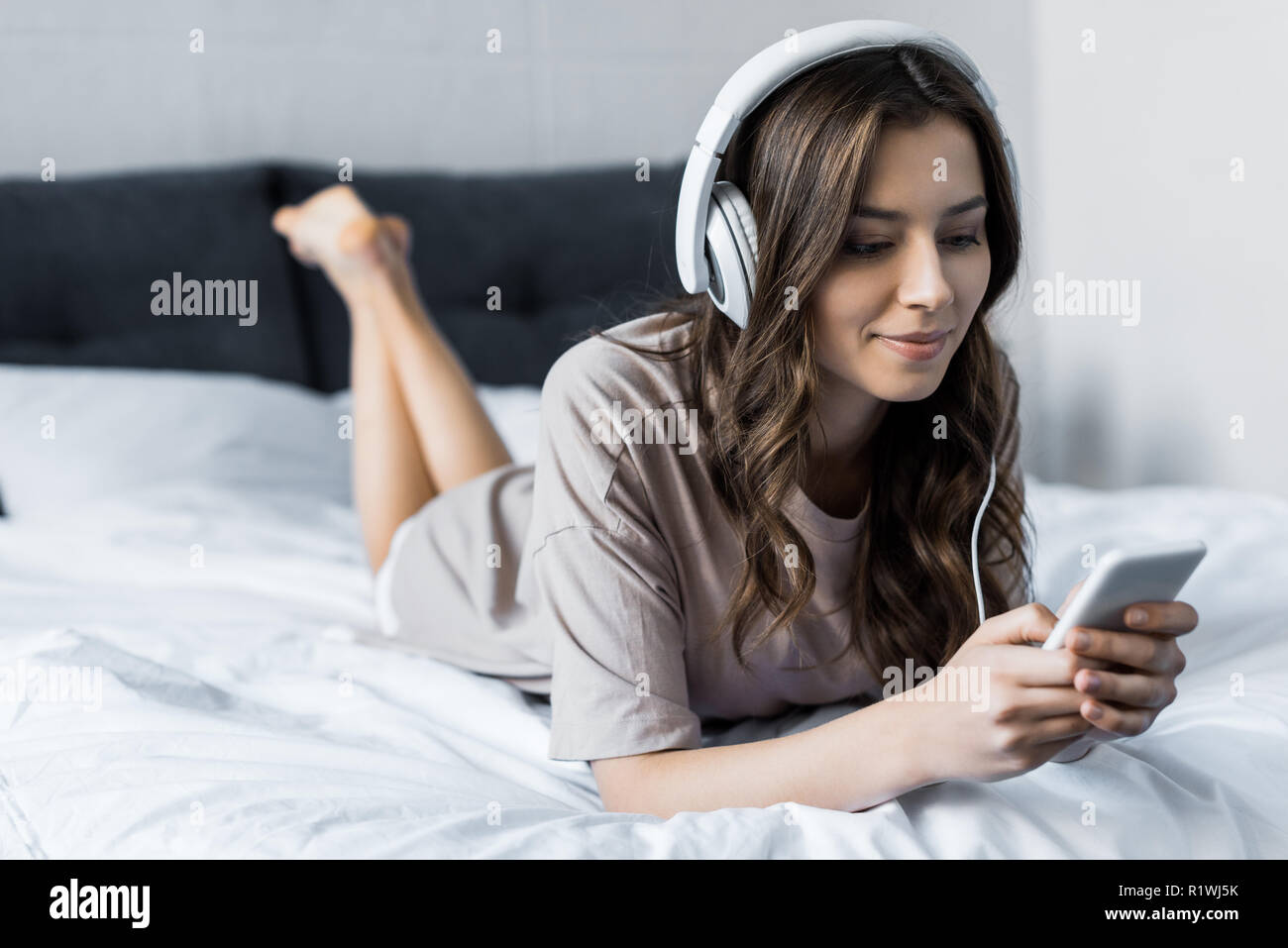 beautiful brunette girl listening music with headphones and smartphone  while lying on bed Stock Photo - Alamy, image size:1300x957