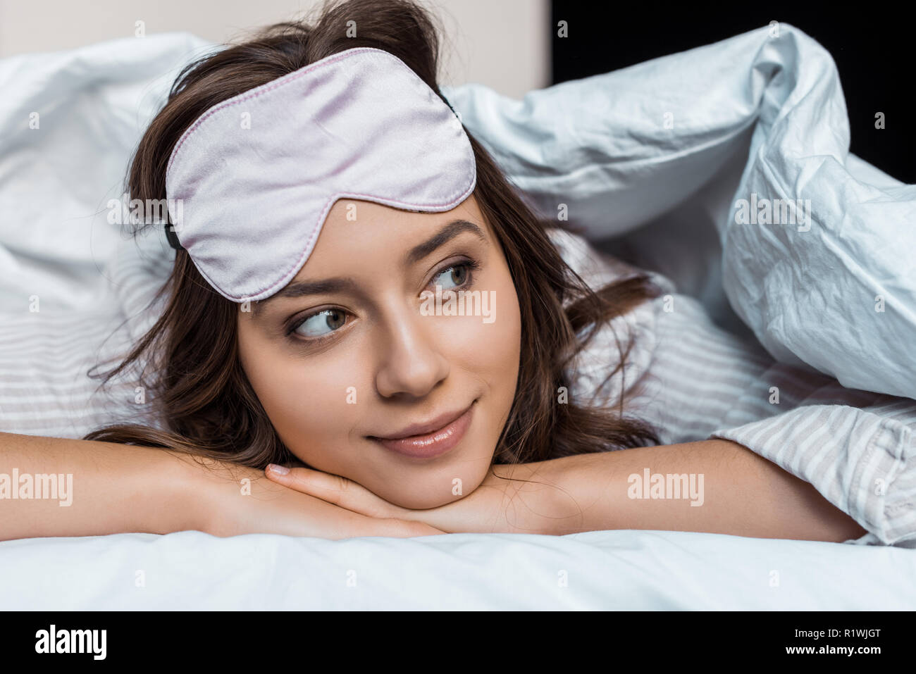 attractive girl in sleeping mask relaxing under blanket on bed Stock Photo