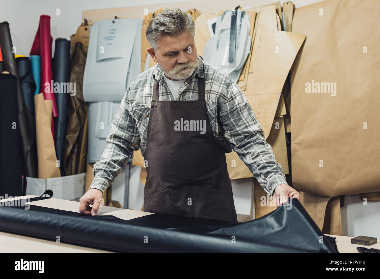mature tailor in apron working with leather at workshop Stock Photo