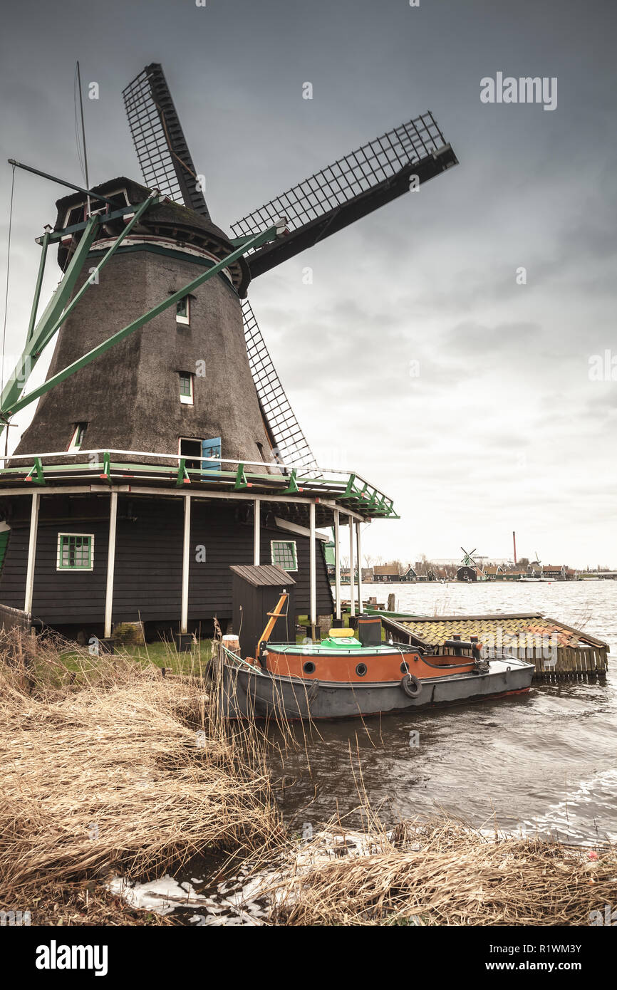 Windmill under dark cloudy sky on Zaan river coast, Zaanse Schans town, popular tourist attractions of the Netherlands. Suburb of Amsterdam Stock Photo