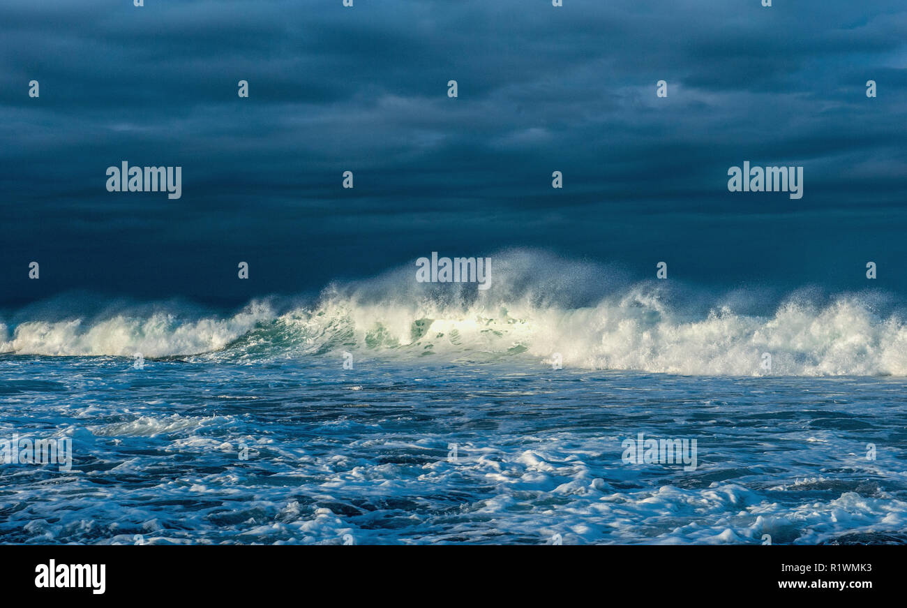 Powerful ocean wave on the surface of the ocean. Wave breaks on a shallow bank. Stormy weather, clouds sky background. Seascape. Stock Photo