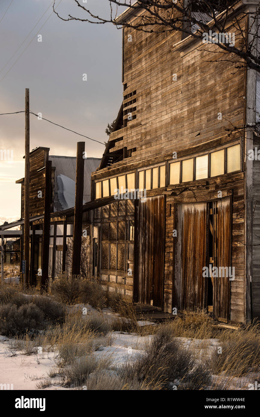 Old wood rustic building with weathered doors and windows and sagebrush, grass and snow in foreground Stock Photo