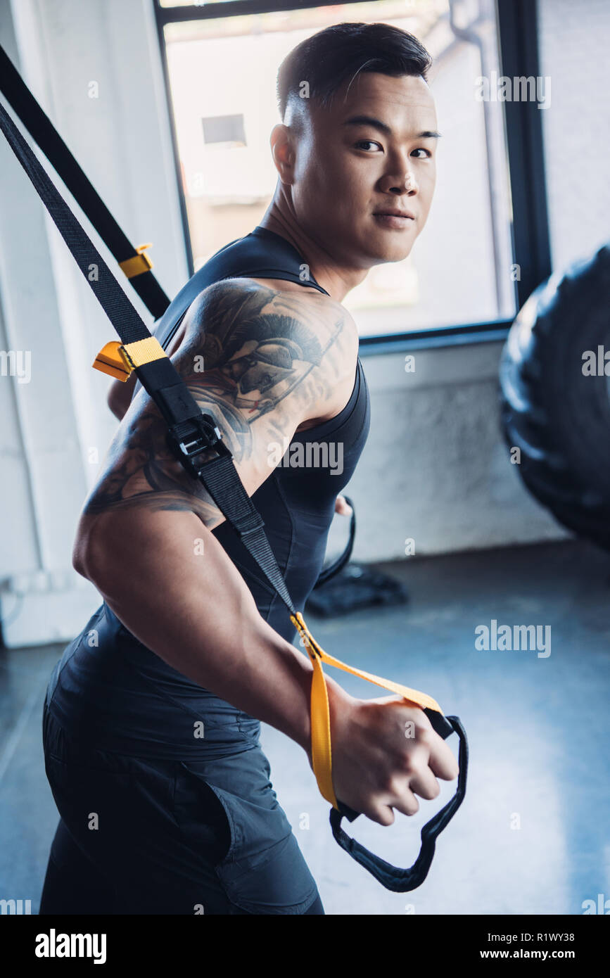 concentrated young asian muscular sportsman training with resistance bands in gym Stock Photo