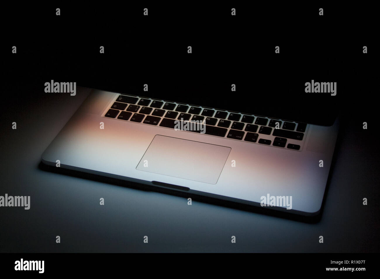 Half closed silver laptop with screen light isolated on dark background Stock Photo