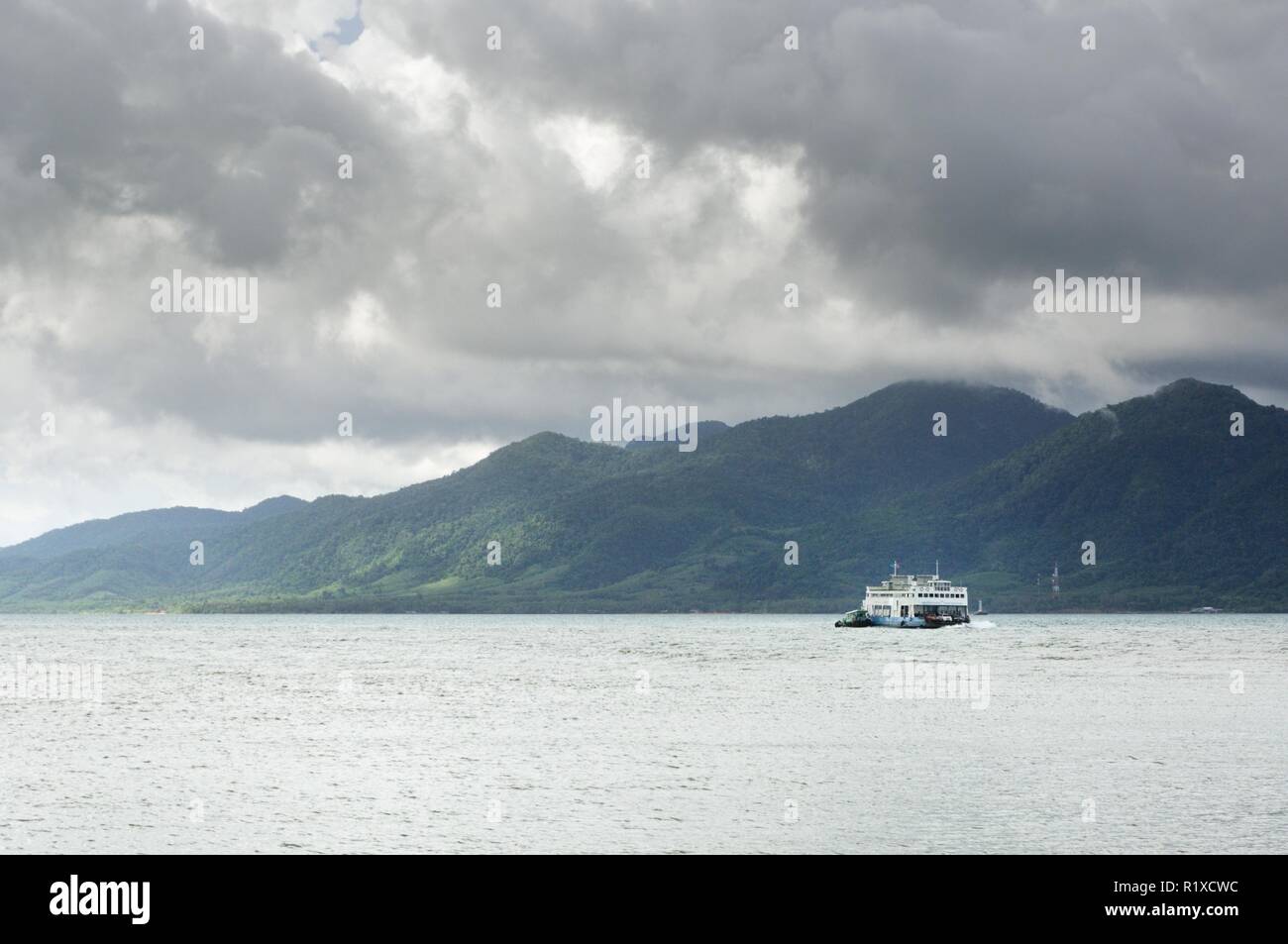 Cargo ferry in tropical sea under monsoon storm heavy clouds and tropical Koh Chang island on horizon in Thailand Stock Photo