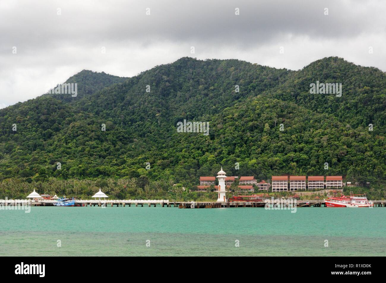 Tropical landscape with turquoise tropical sea, white lighthouse, fishing boat, Bang Bao pier and tropical Koh Chang Island on horizon in Thailand Stock Photo