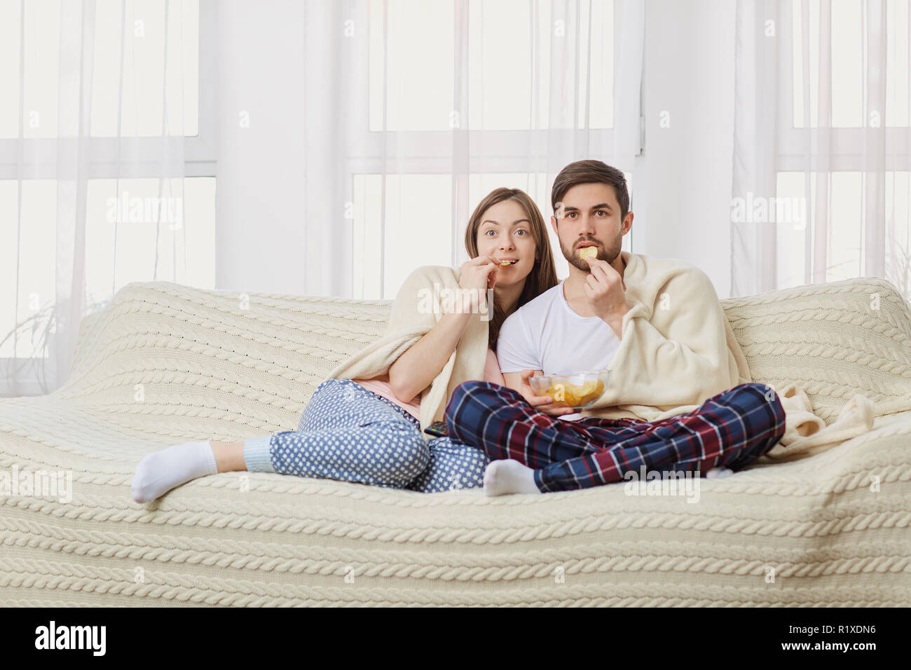 A young couple sitting on the couch watching an interesting TV . Stock Photo