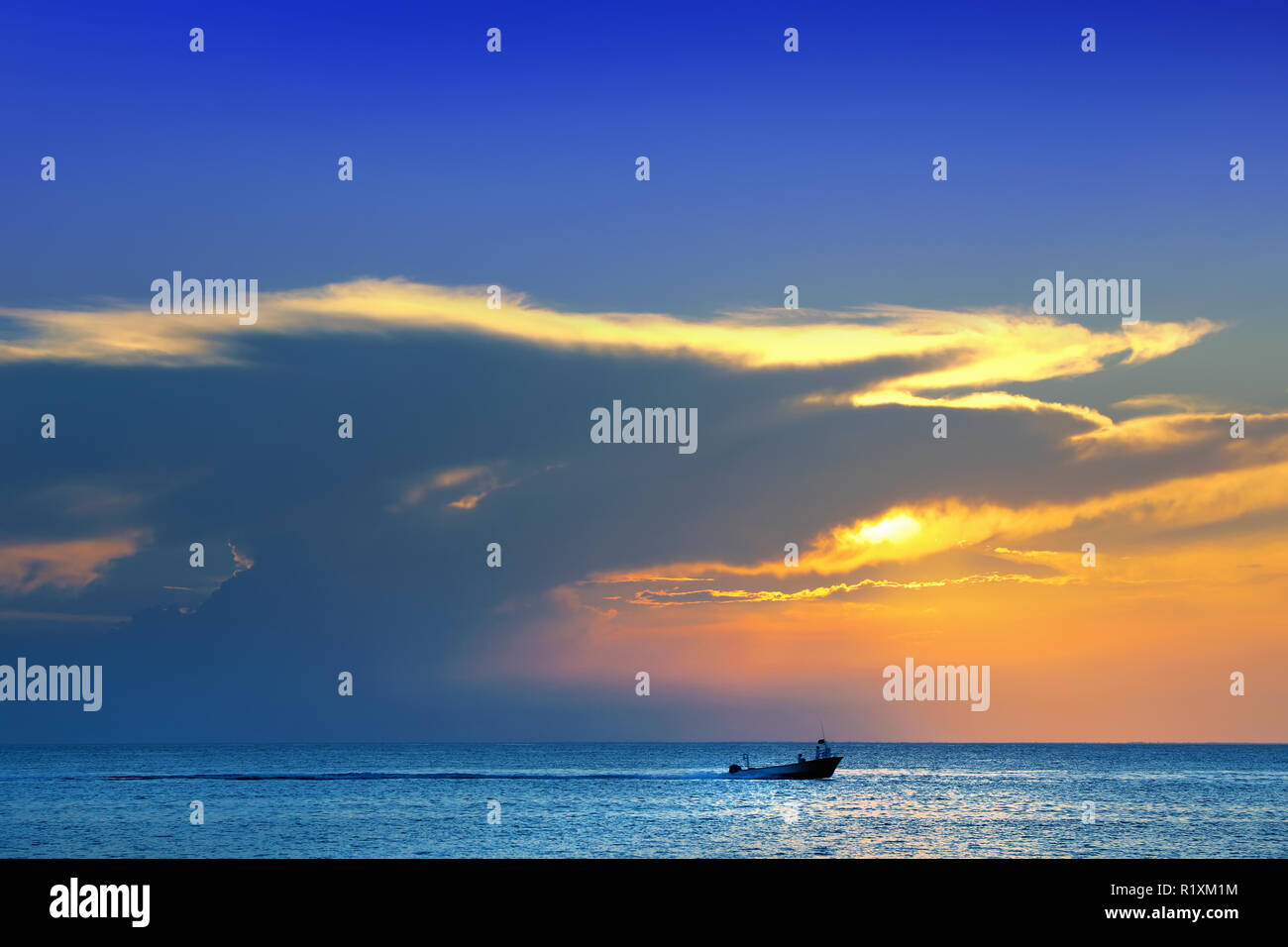 Colorful seascape image with shiny sea and speedboat over cloudy sky and sun during sunset in Cozumel, Mexico Stock Photo
