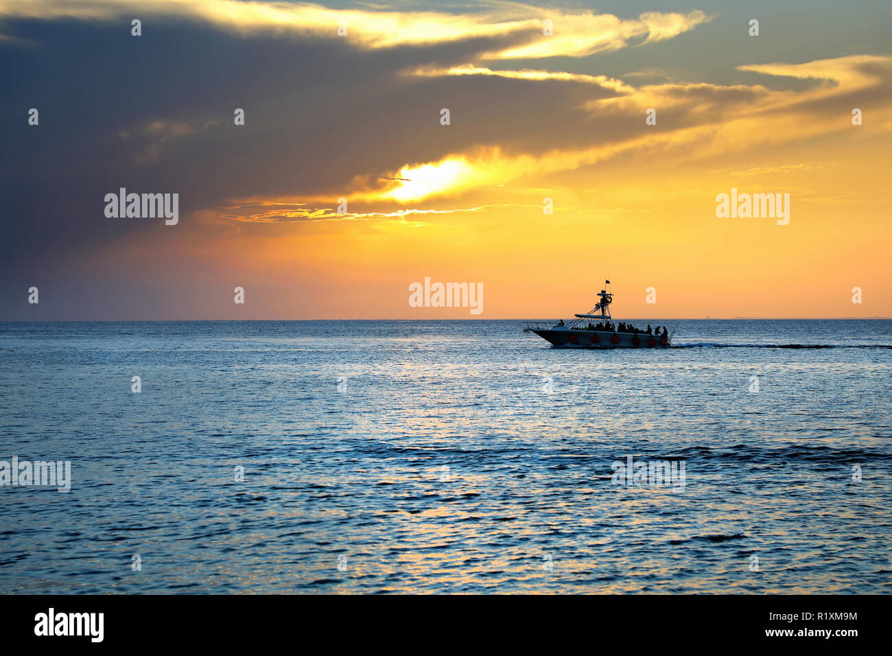 Colorful seascape image with shiny sea and speedboat over cloudy sky and sun during sunset in Cozumel, Mexico Stock Photo