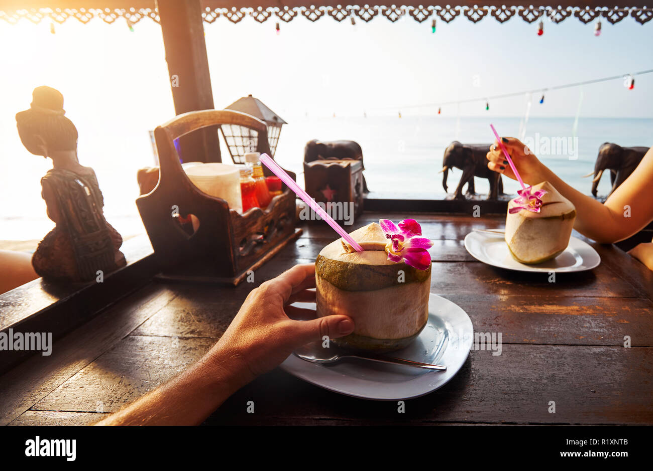 Couple drinks sweet fresh coconuts decorated with flower at restaurant on the beach at sunrise Stock Photo