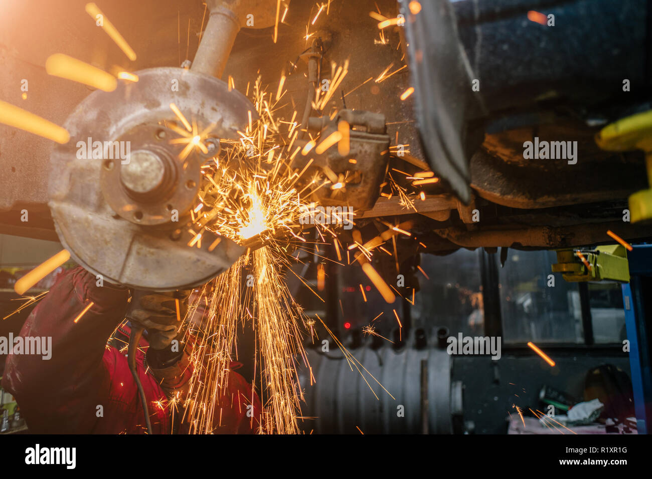 Young caucasian man in red work clothing repairing car with angle cutter. Many sparks on background. Stock Photo