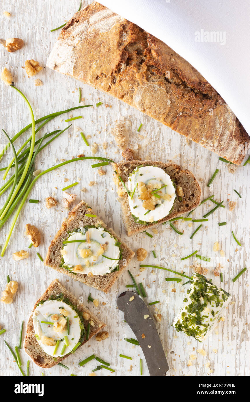 Frisches Landbrot und Schnittchen mit Frischkäse Schnittlauch und Walnüssen auf hellen Holzuntergrund Stock Photo