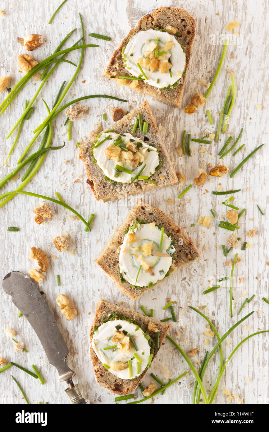 Frisches Landbrot und Schnittchen mit Frischkäse Schnittlauch und Walnüssen auf hellen Holzuntergrund Stock Photo