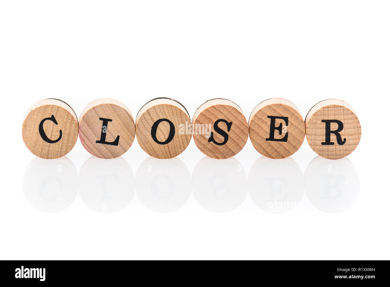 Word Closer from circular wooden tiles with letters children toy. Concept of nearness spelled in children toy letters. Stock Photo
