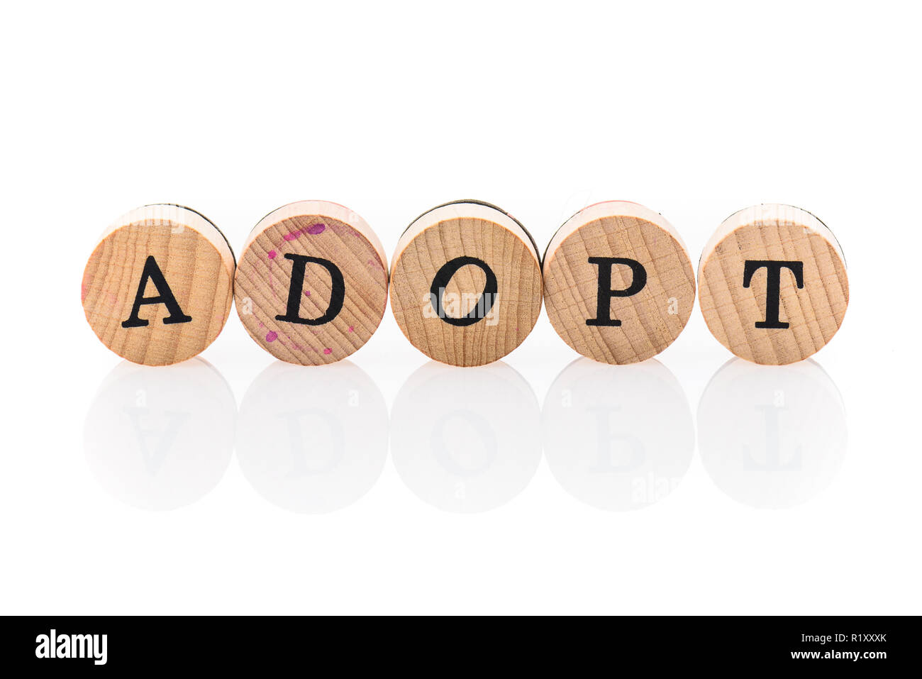 Word Adopt from circular wooden tiles with letters children toy. Concept of adoption spelled in children toy letters. Stock Photo