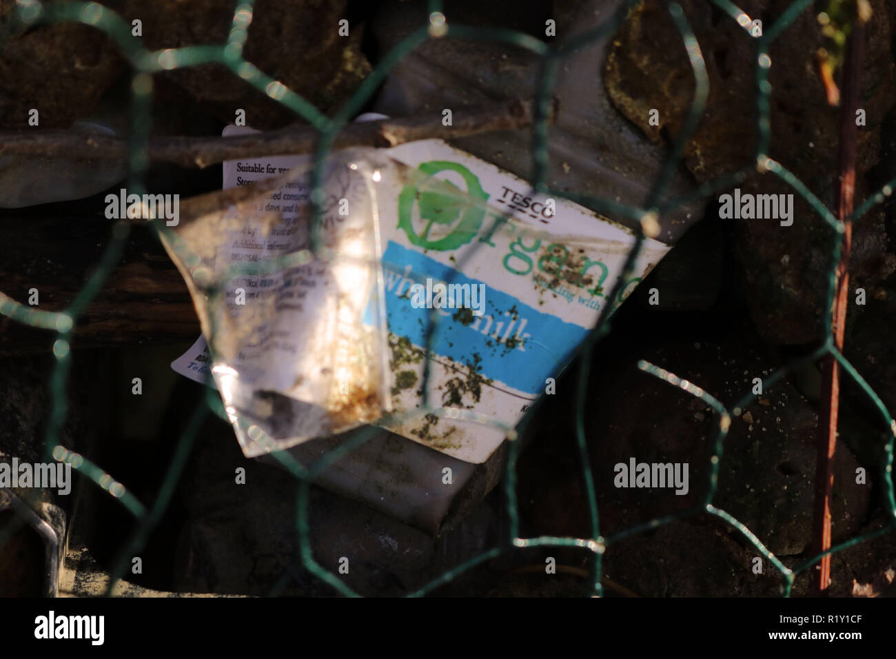 Plastic milk bottle found in the River Thames to show the high use of Plastic used in the environment, shot behind green wire. Stock Photo
