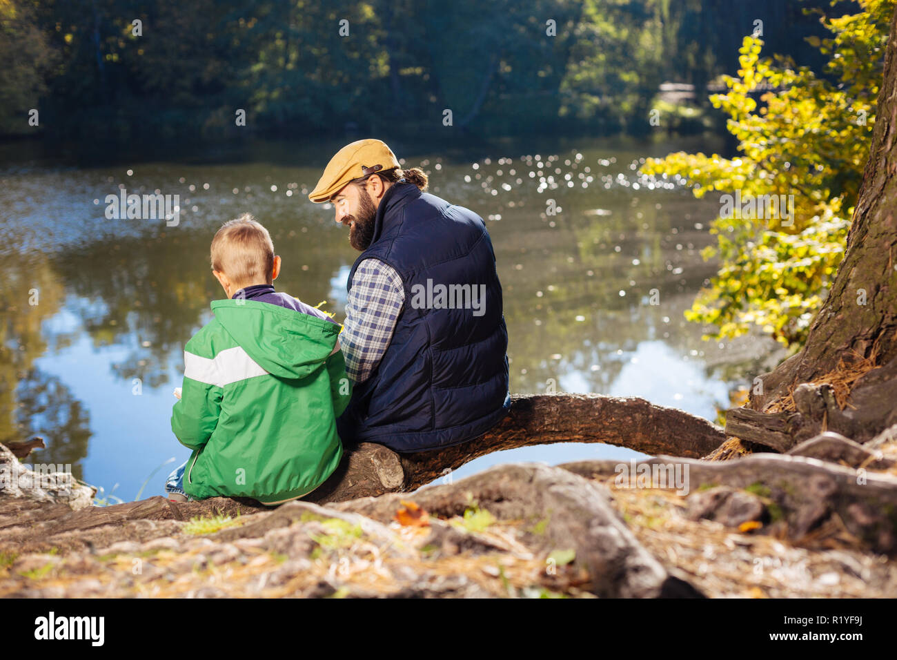 Nice positive man and boy sitting on the tree root Stock Photo