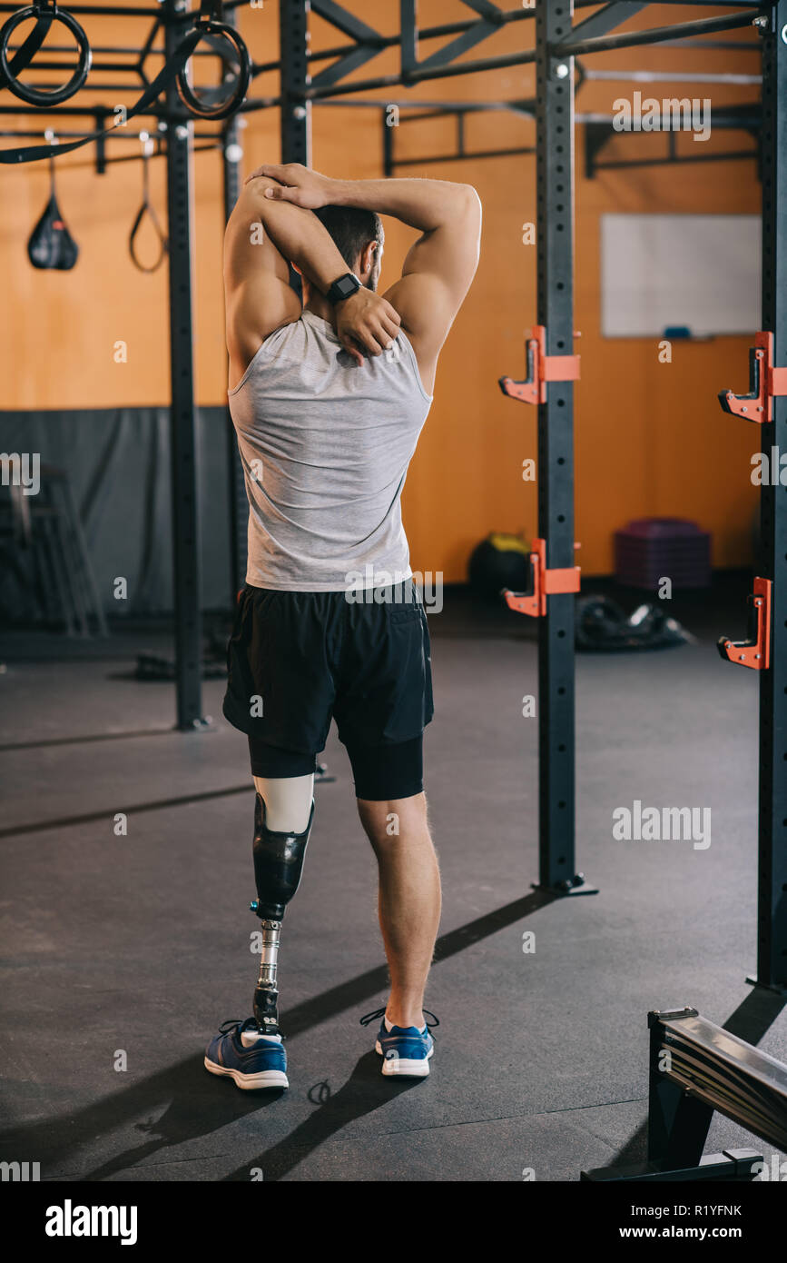 rear view of young sportsman with artificial leg stretching near