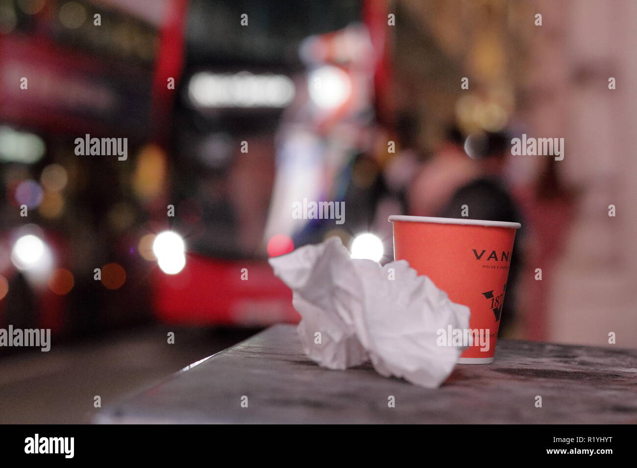 Night shot in London with famous red busses on the background with rubbish left on the street. Coffee cup and folded paper. Stock Photo