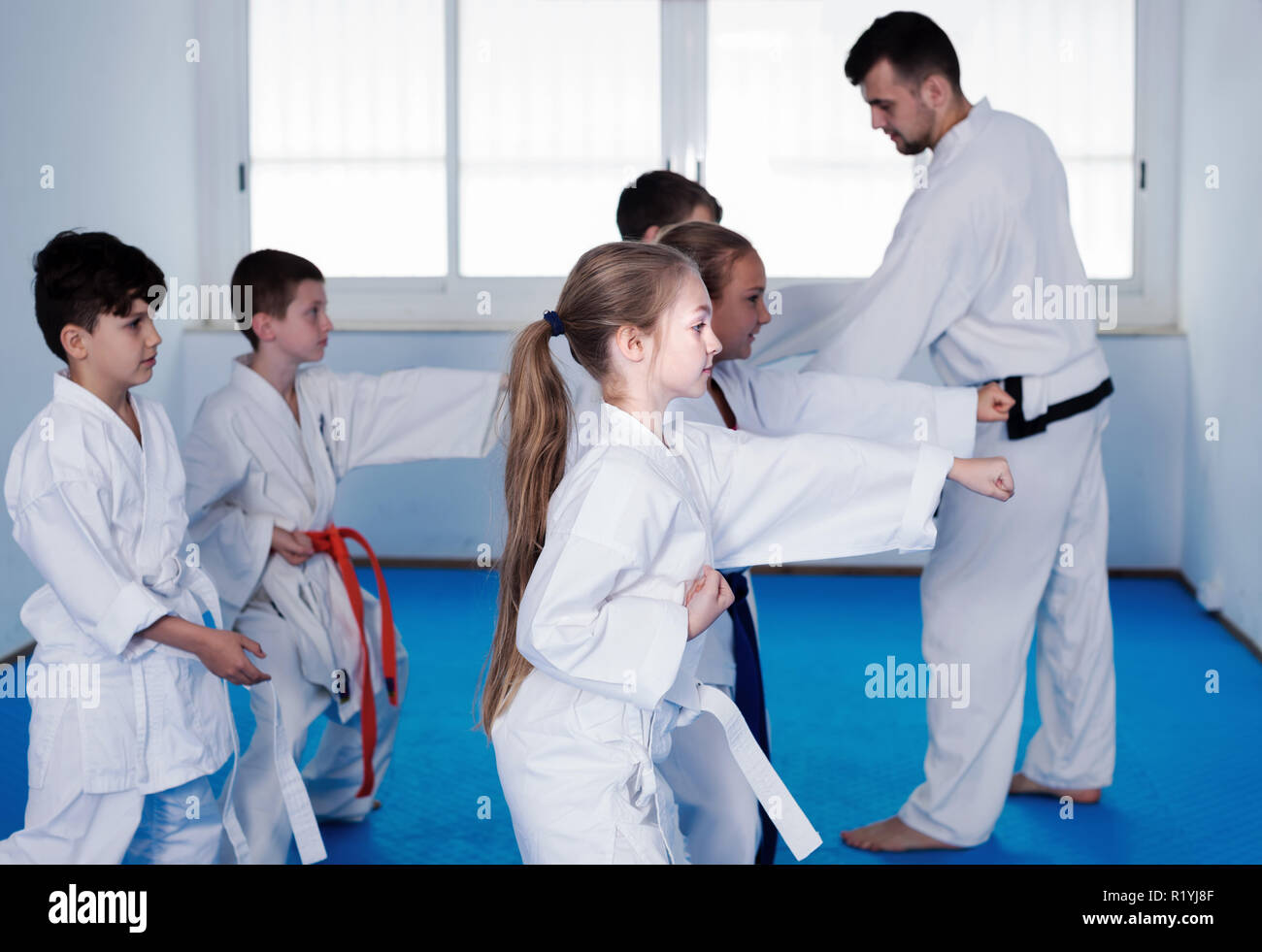 Young children practice karate kicks with male coach during karate class Stock Photo