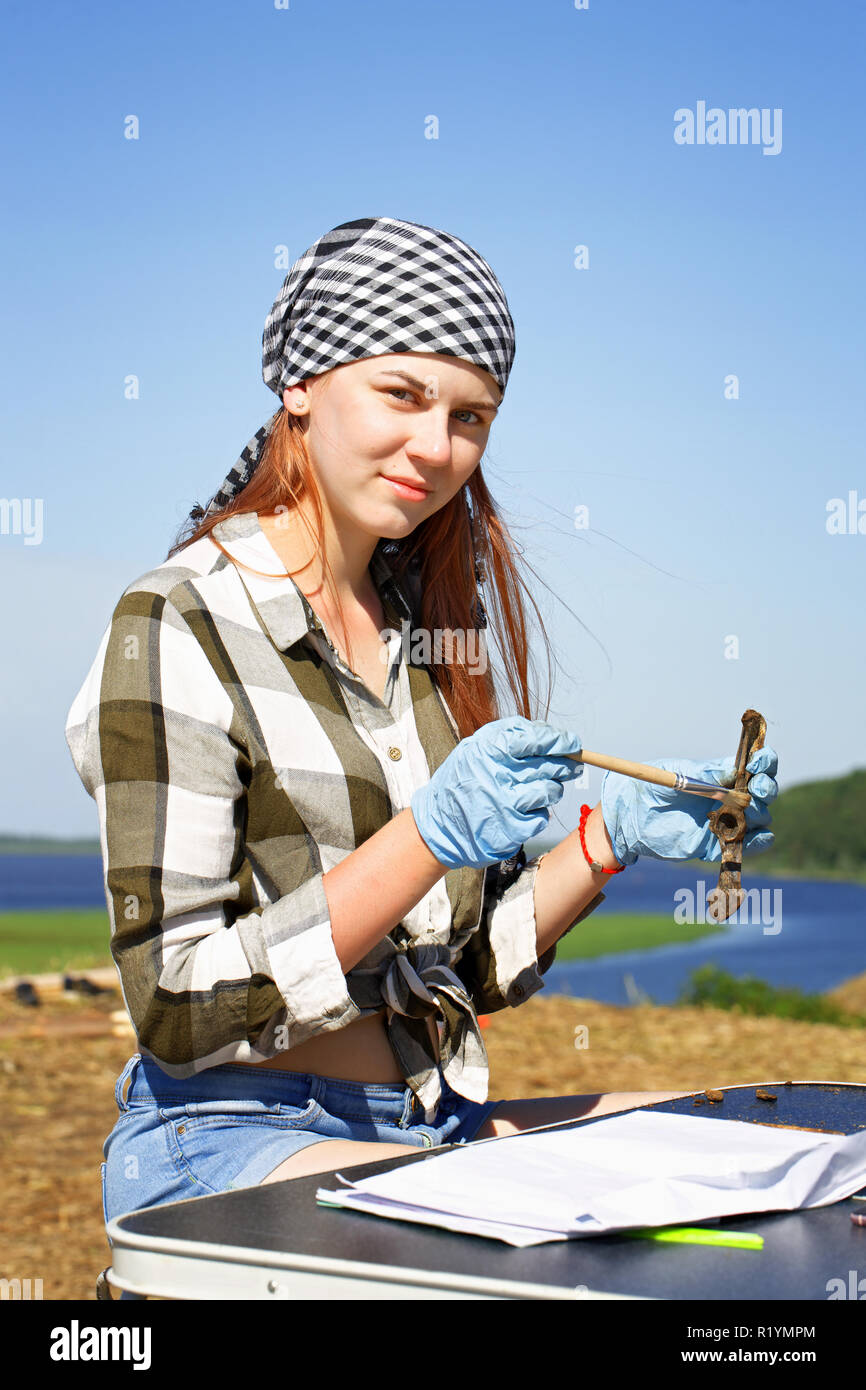 Beautiful girl archaeologist carefully cleans the find - part of the spine of a medieval mammal. The pleasure of working in a field expedition Stock Photo