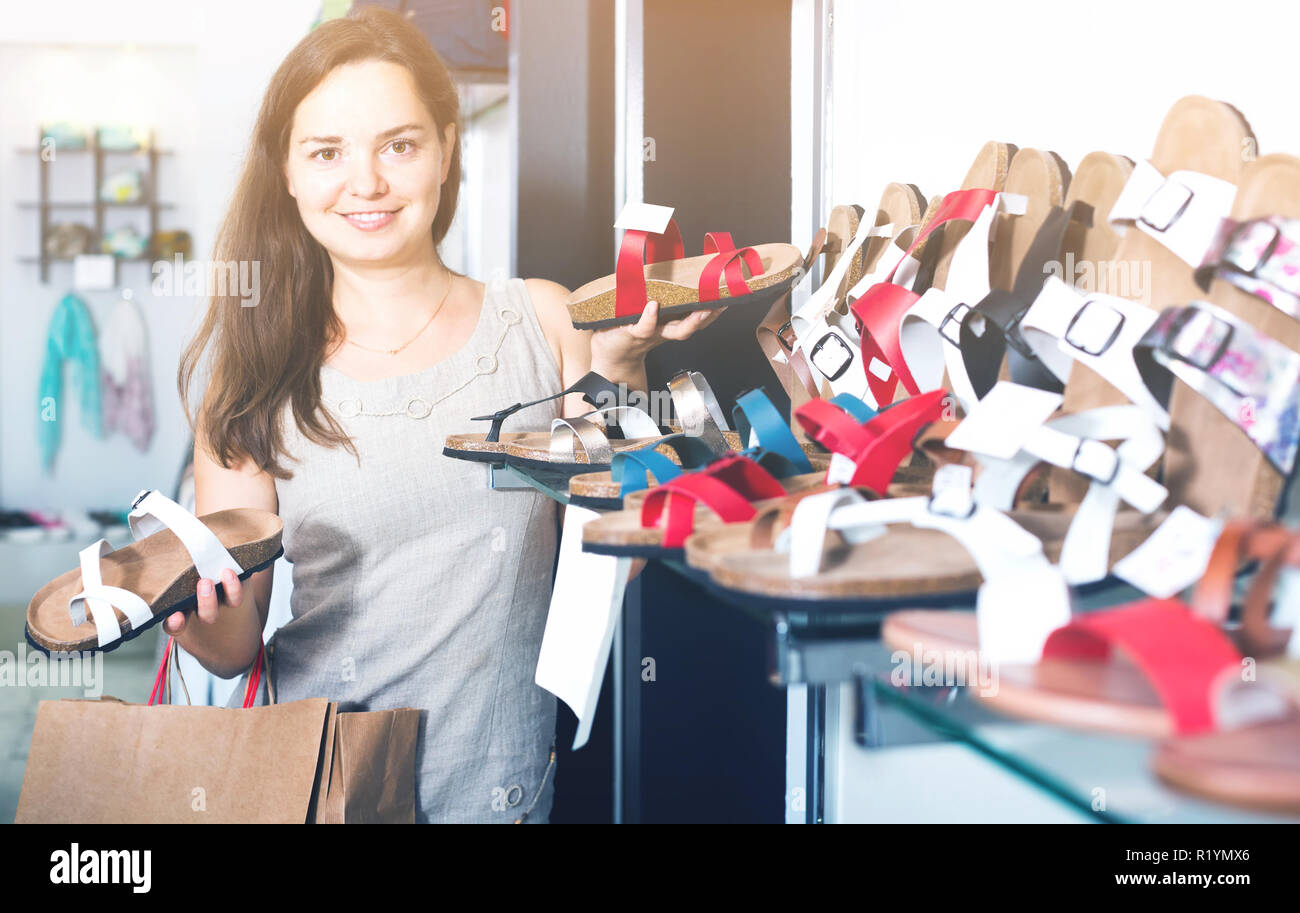 smiling young darkhaired woman choosing summer sandals in shoes store Stock Photo