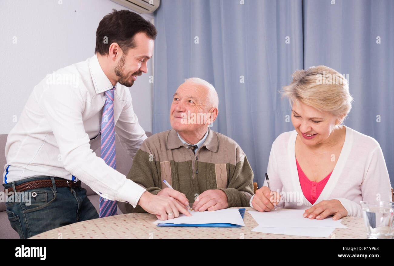 ature woman and her eldery father signing contract with smiling sales manager at home Stock Photo