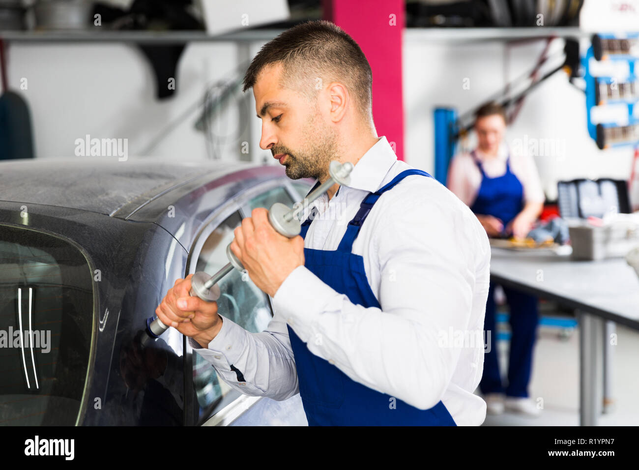 Concentrated mechanic performing car body repair at auto workshop with tools for repairing dents Stock Photo