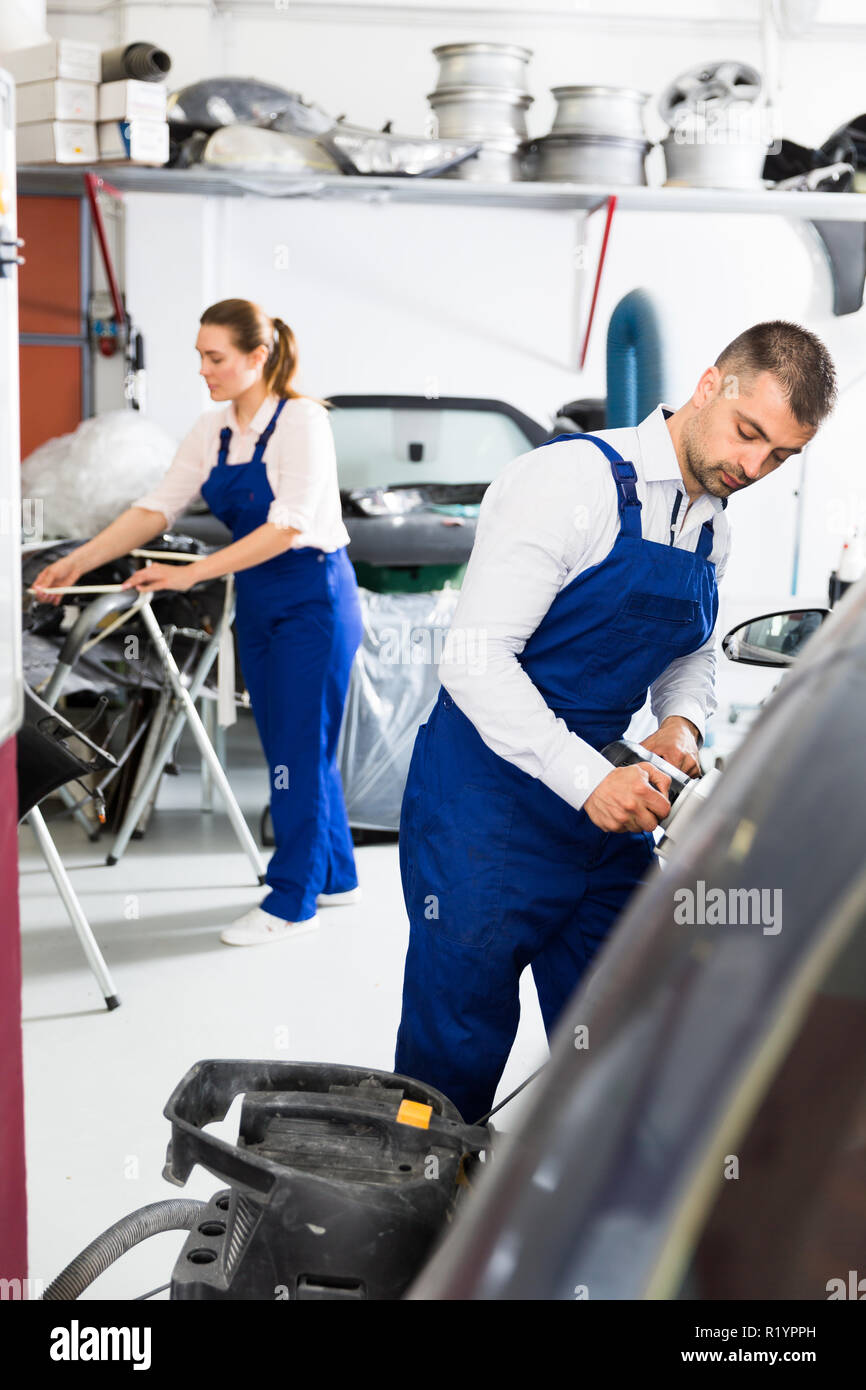 Serious male worker in auto repair shop grinding body car before painting Stock Photo