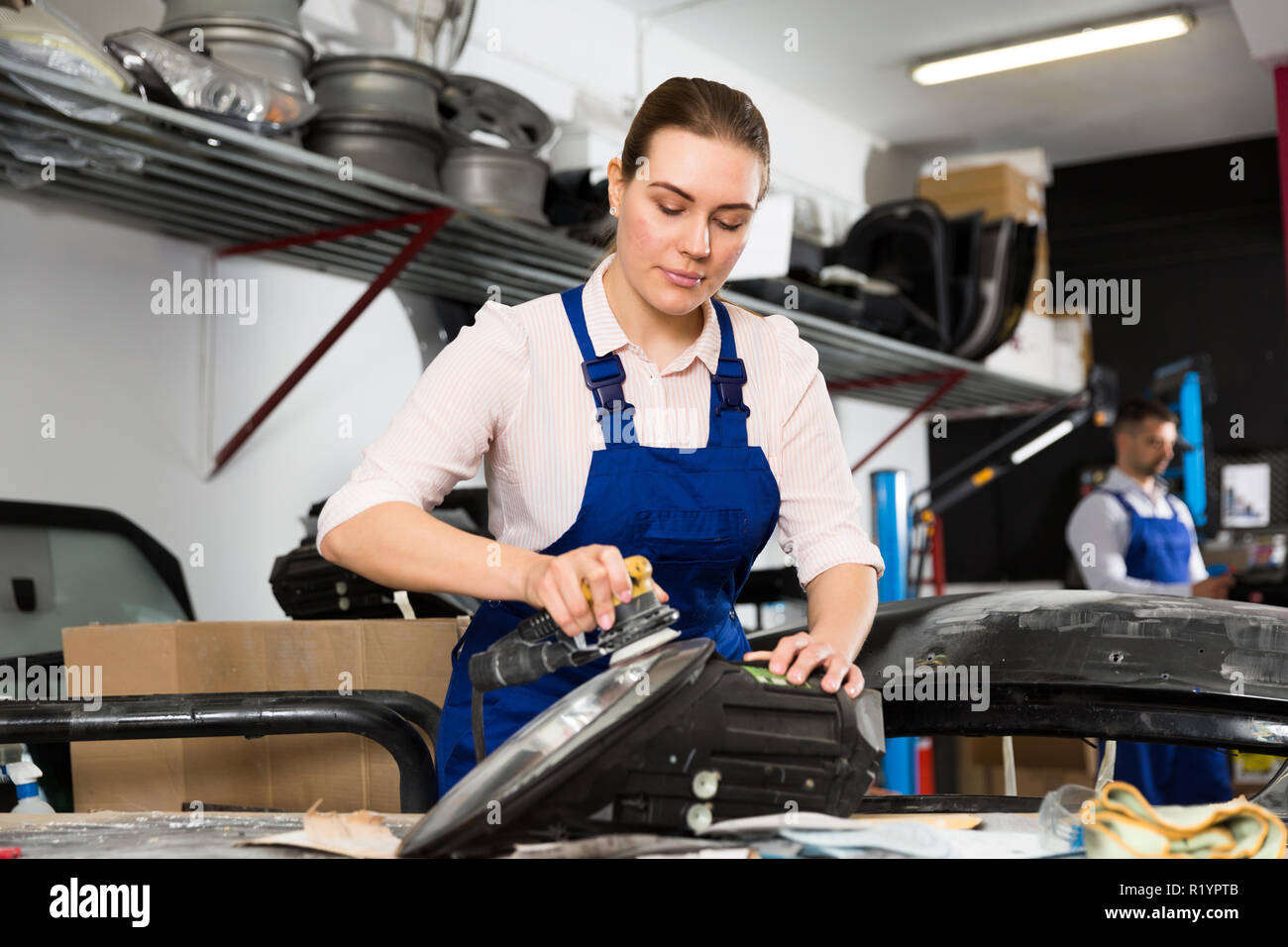 Professional female worker polishing headlamp in auto repair shop Stock Photo