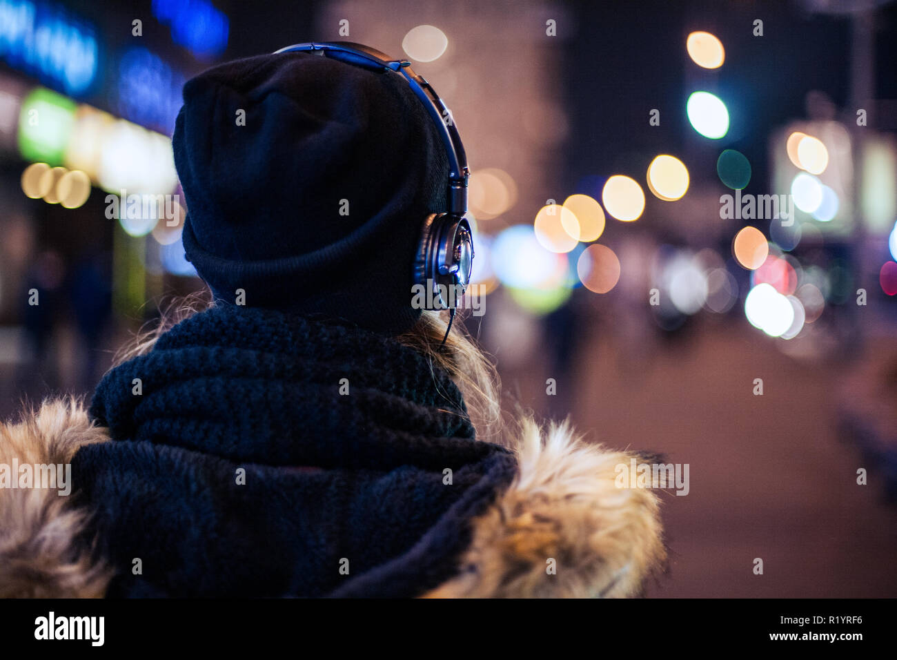 Back view of a hipster girl walking through night city street listening ...
