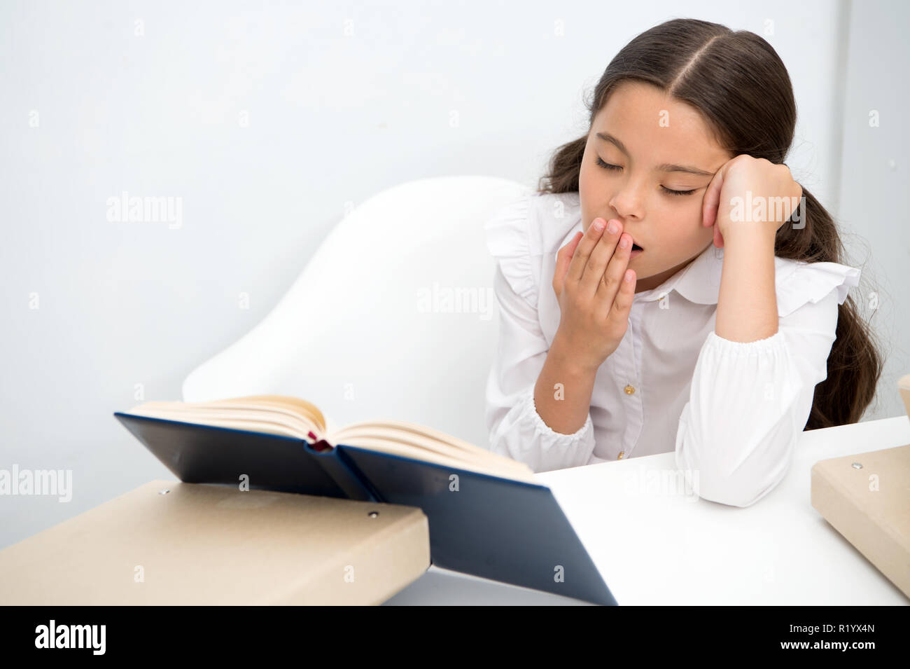 Boring literature. Girl child reads book while sit table white