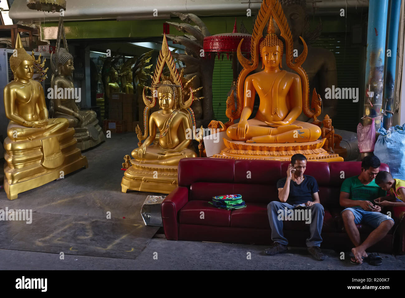 After working hours, workers and a child relax in a factory for Buddha statues and other religious objects in Bamrung Muang Road., Bangkok, Thailand Stock Photo