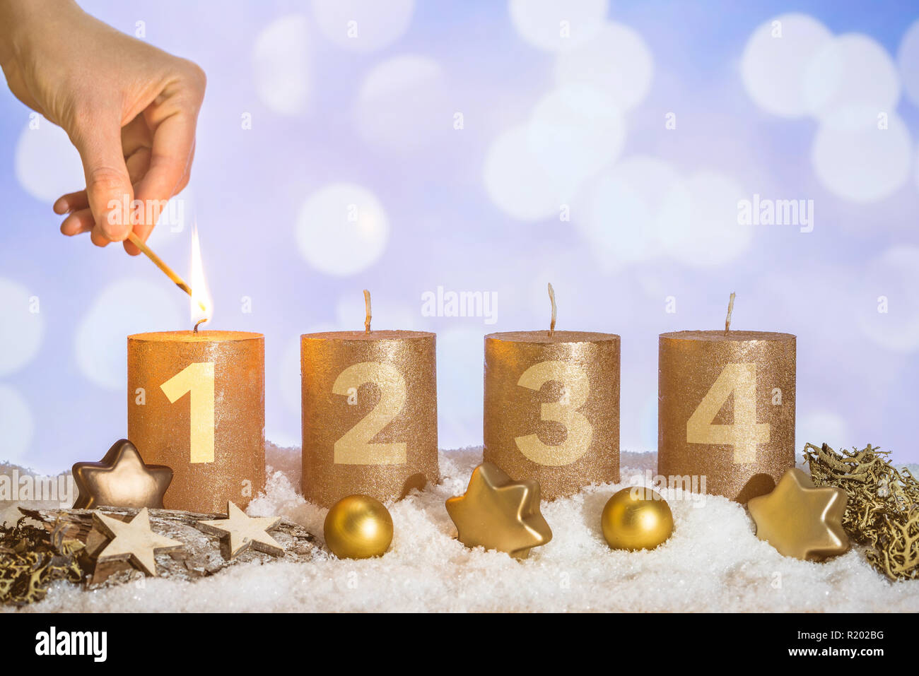 Four numbered gold advent candles with first candle lit by hand with match  and christmas decoration lying in snow as template Stock Photo - Alamy