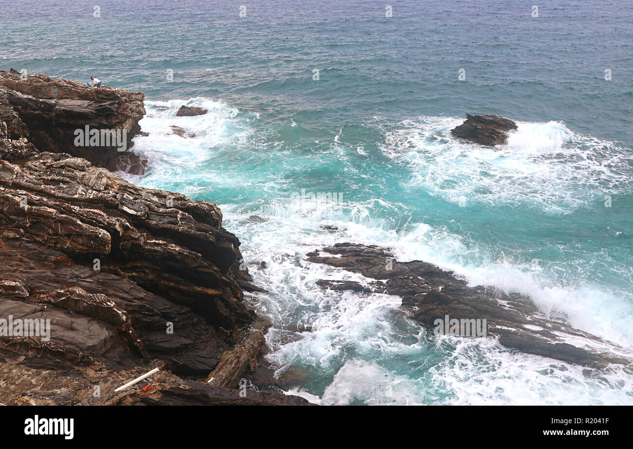 Stormy weather and breaking waves to the cliffs of the coastline of Genoa-Nervi, with a solitary fisher on the top Stock Photo