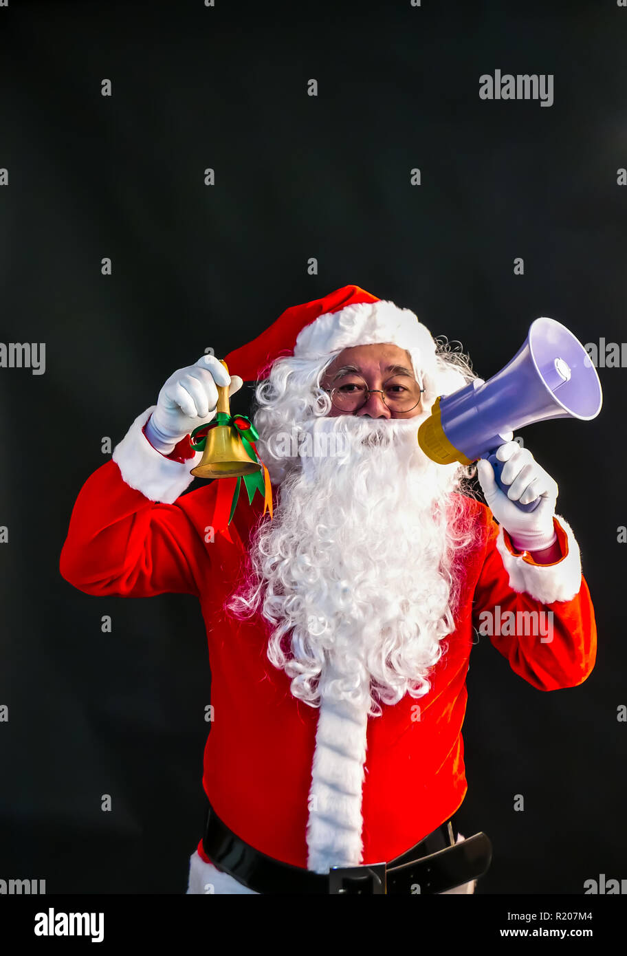 Santa Claus speaks on megaphone on his right hand & ring a bell on his lift hand studio shot on black background for family, giving, season, Christmas Stock Photo