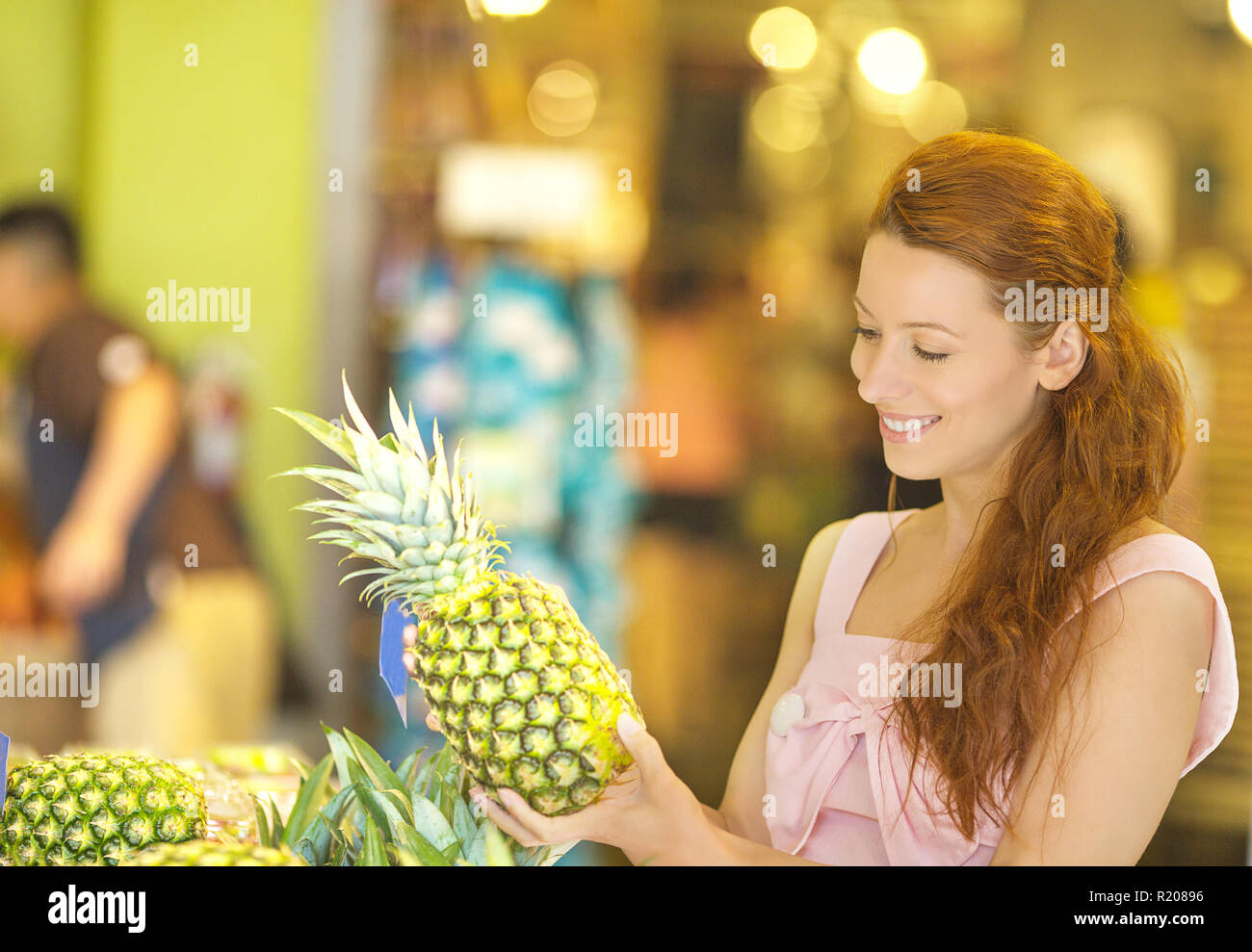 Charming young woman choosing pineapple while shopping in grocery store Stock Photo