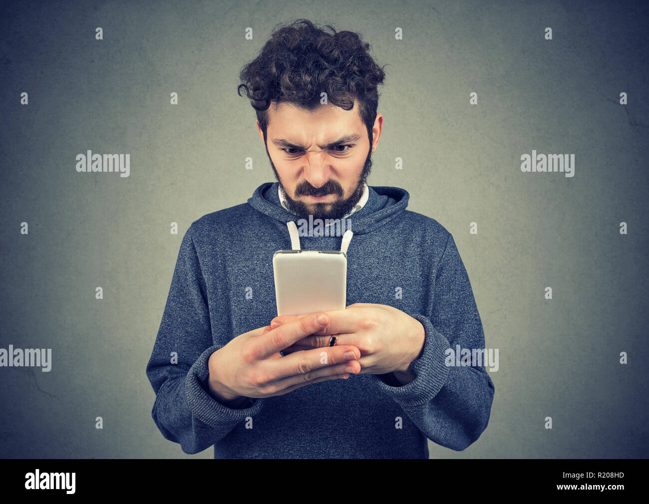 Young bearded man holding smartphone being upset with text message Stock Photo