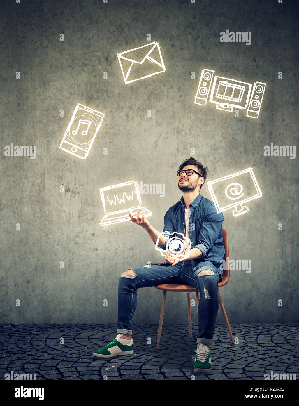 Funny skillful man sitting on chair and juggling with electronic devices icons Stock Photo
