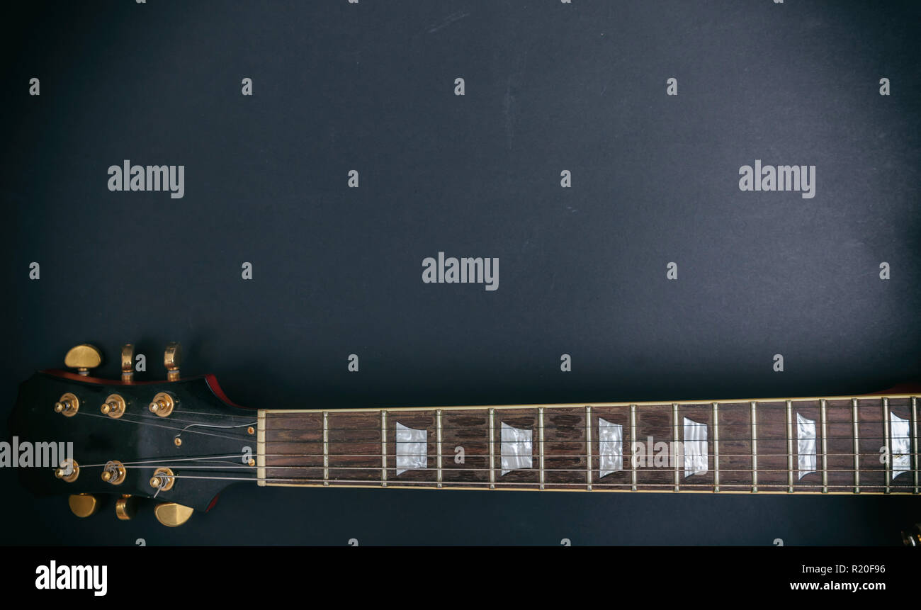 Music, guitar. Top view of a guitar neck fretboard and headstock against black background, copy space. Stock Photo