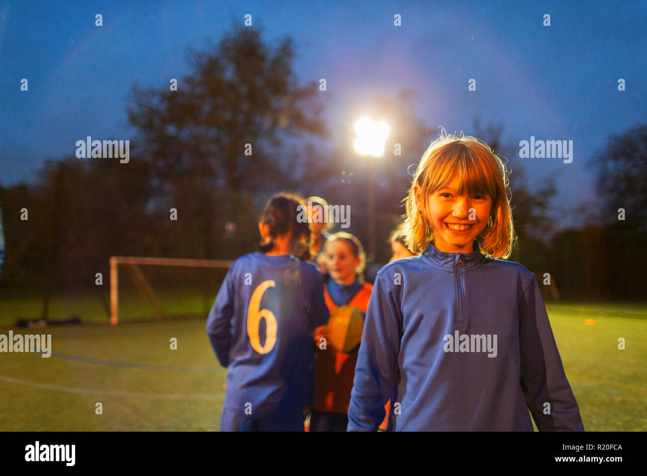 Portrait confident girl playing soccer with team on field at night Stock Photo