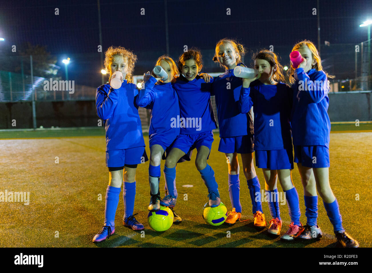 Portrait confident girls soccer team drinking water on field at night Stock Photo