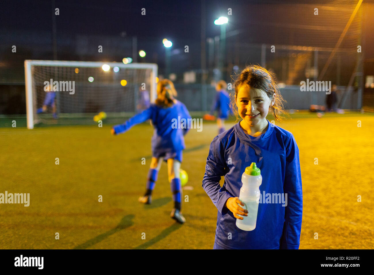 Portrait smiling girl soccer player drinking water on field at night Stock Photo