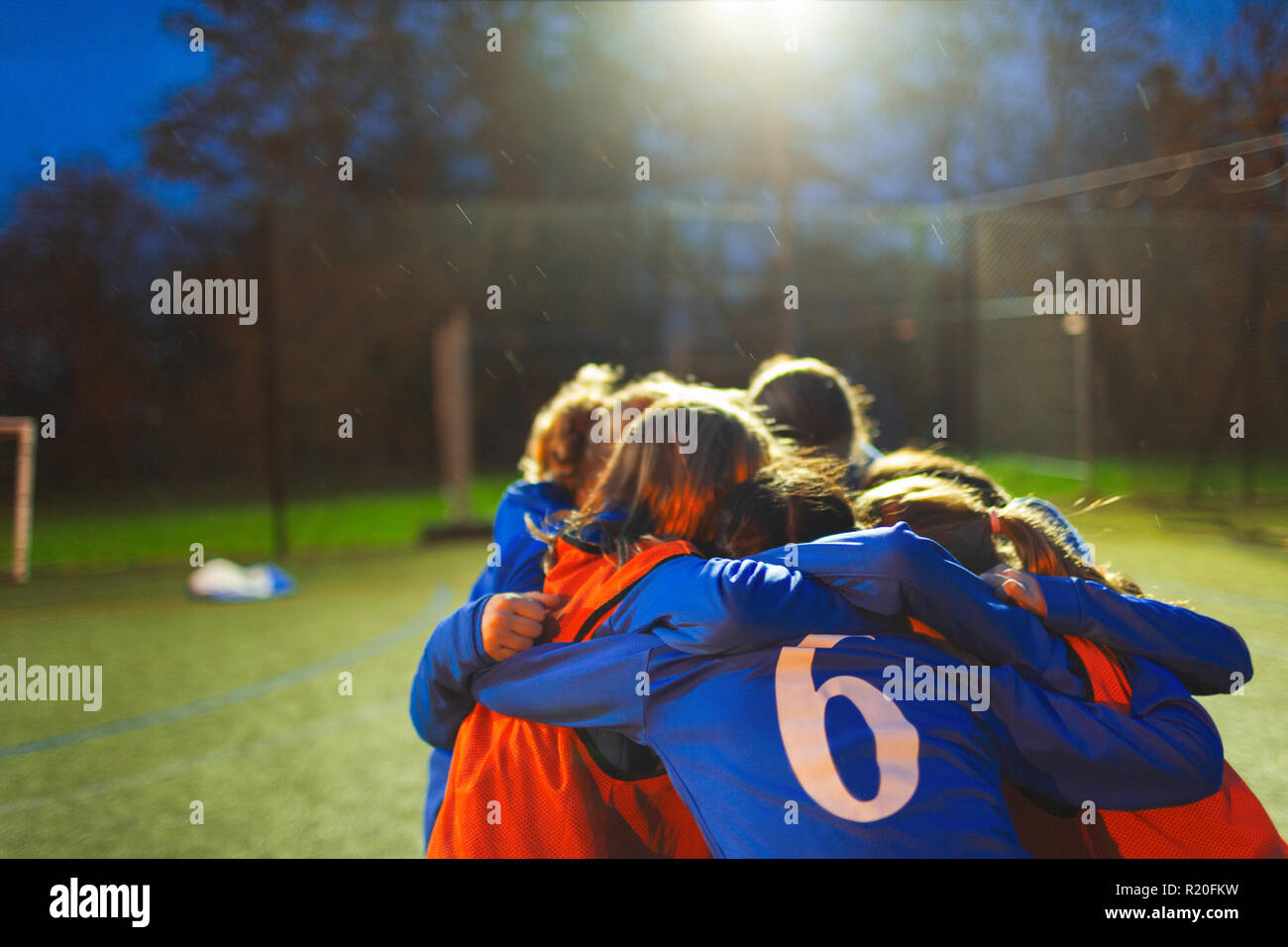 Girls soccer team huddling on field at night Stock Photo